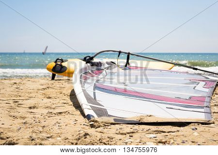 Windsurfing board with sail lying on the sand and windless sea