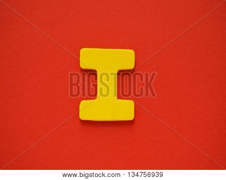 Capital letter I. Yellow letter I from wood on red background. Alphabet vowel.