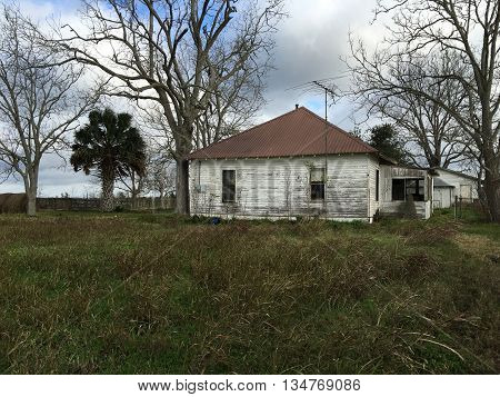 Old house in a field behind a broken picket fence.