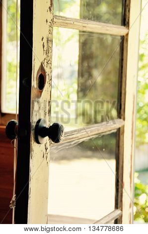 A door knob on an old beat up glass door that is open.