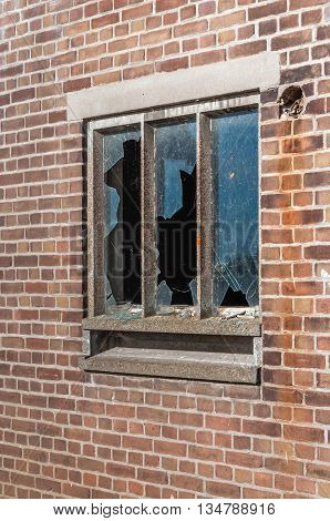 Broken glass panes of an old window in the concrete frame of a masonry brick wall. It now looks a bit mysterious and creepy.