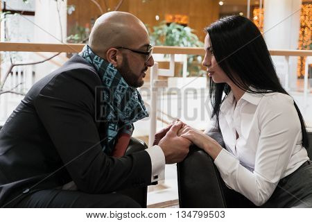Arab man and the stylish girl sitting and holding hands in an airport lounge