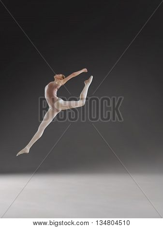 Young beautiful ballerina posing in jump in studio