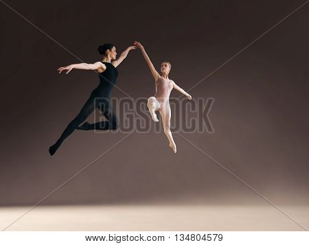 Two ballet dancers jumping high in air on gray blackground