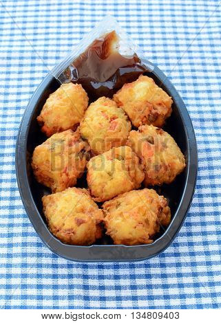 Fresh vegetable pakoras with tamarind chutney prepared by the delicatessan in plastic container on blue and white check cloth in vertical format