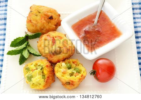 Fresh vegetable pakoras with sweet chili sauce on square white plate on blue and white check cloth in horizontal format