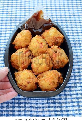 Fresh vegetable pakoras with tamarind chutney prepared by the delicatessan in plastic container on blue and white check cloth in vertical format with hand