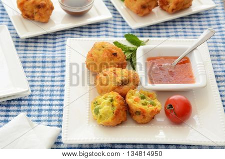 Fresh vegetable pakoras with sweet chili sauce on square white plate on blue and white check cloth in horizontal format