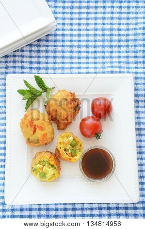 Fresh vegetable pakoras with tamarind chutney on square white plate on blue and white check cloth in vertical format