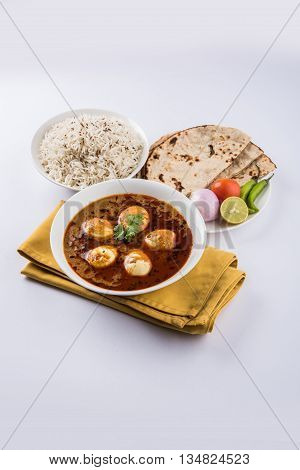 egg curry with roti/chapati and jeera rice, tasty and spicy anda curry with roti and rice, indian egg masala curry served in ceramic bowl with roti, salad and jeera rice