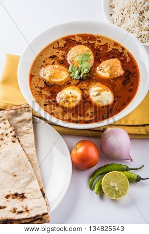egg curry with roti/chapati and jeera rice, tasty and spicy anda curry with roti and rice, indian egg masala curry served in ceramic bowl with roti, salad and jeera rice