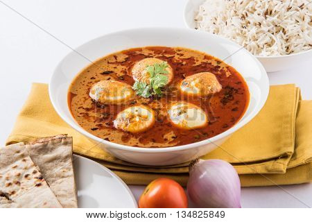 egg curry with roti/chapati and jeera rice, tasty and spicy anda curry with roti and rice, indian egg masala curry served in ceramic bowl with roti, salad and jeera rice