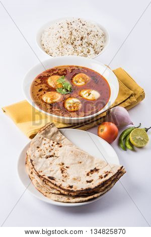 egg curry with roti/chapati and jeera rice, tasty and spicy anda curry with roti and rice, indian egg masala curry served in ceramic bowl with roti, salad and jeera rice