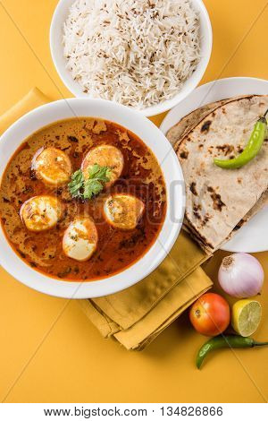 egg curry with roti/chapati and jeera rice, tasty and spicy anda curry with roti and rice, indian egg masala curry served in ceramic bowl with roti, salad and jeera rice