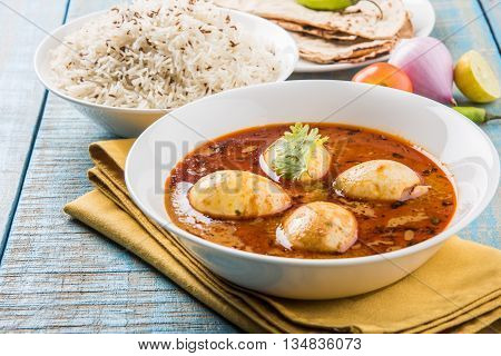 egg curry with roti/chapati and jeera rice, tasty and spicy anda curry with roti and rice, indian egg masala curry served in ceramic bowl with roti, salad and jeera rice