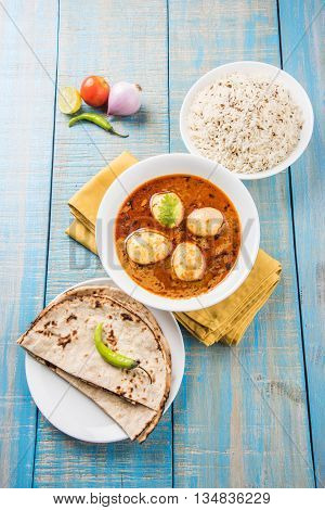 egg curry with roti/chapati and jeera rice, tasty and spicy anda curry with roti and rice, indian egg masala curry served in ceramic bowl with roti, salad and jeera rice