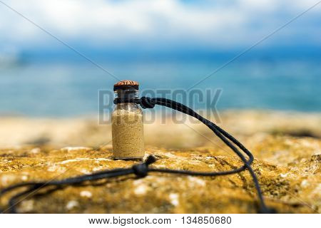 Vial with white sand like memory about tropical vacation. Sea and blue sky background