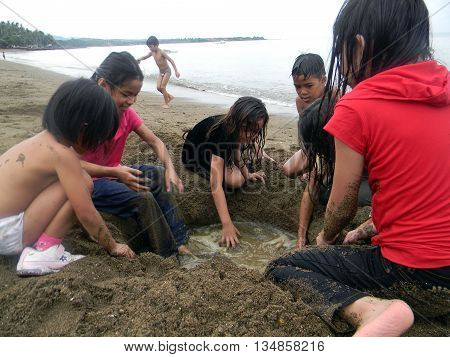 CEBU CITY, CEBU / PHILIPPINES - JULY 30, 2011: Children dig a hole in the sand at a public beach in Cebu.