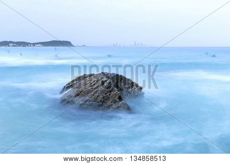 Twilight at Currumbin Rock Gold Coast with ocean current rushing against a large rock on overcast morning.