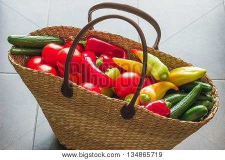 Wicker shopping bag filled with fresh vegetables from the market. Bright tomatoes cucumbers and peppers.