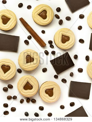 A seamless background pattern with pieces of chocolate cocoa cookies with heart-shaped fillings coffee beans and a cinnamon stick scattered on white background