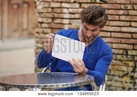 Young man using tablet pc as a mirror to fix his hair in outdoor cafe