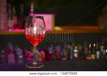 Red cold cocktail on bar counter against of shelves with bottles. Bokeh