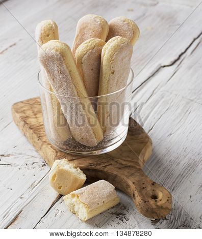 Sweet pastries, biscuits Savoiardi, ladies fingers in a glass mug on a light plain wooden background. selective focus