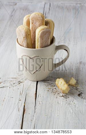 Sweet pastries, biscuits Savoiardi, ladies fingers in a glass mug on a light plain wooden background. selective focus