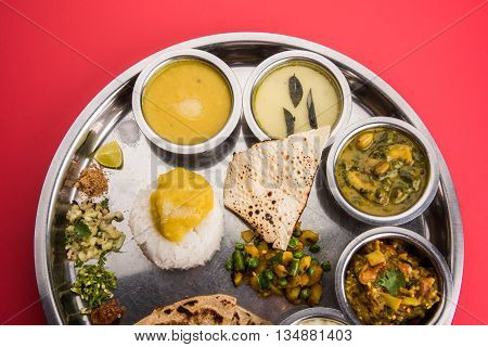 typical maharashtrian food served in a steal plate, marathi food includes kadhi and shrikhand, plain dal, spinach curry, aalu mutter, plain rice, papad, bhakri or bhakar or roti and variety of salad