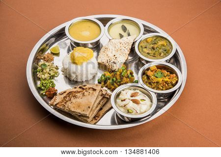 typical maharashtrian food served in a steal plate, marathi food includes kadhi and shrikhand, plain dal, spinach curry, aalu mutter, plain rice, papad, bhakri or bhakar or roti and variety of salad