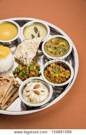 typical maharashtrian food served in a steal plate, marathi food includes kadhi and shrikhand, plain dal, spinach curry, aalu mutter, plain rice, papad, bhakri or bhakar or roti and variety of salad