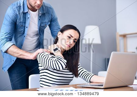 I need massage. Pleasant cheerless sick woman having an ache in neck and using laptop while the boyfriends holding hand on her shoulders
