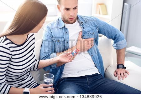 Unexpected pain. Handsome sick man having a heartache while her girlfriend helping him and giving medicines