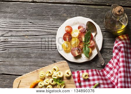 Healthy snack. White ceramic dish with a salad of multicolored cherry tomatoes with olive oil on a dark wooden background. Served for dinner with pasta tagliatelle on the board of the olive tree.