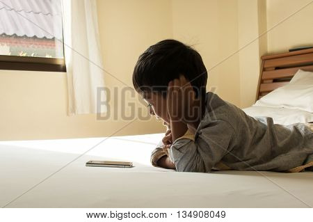 little boy laying on bed playing with smart phone in bedroom