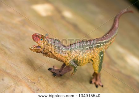 a brown carnotaurus toy stands on rock