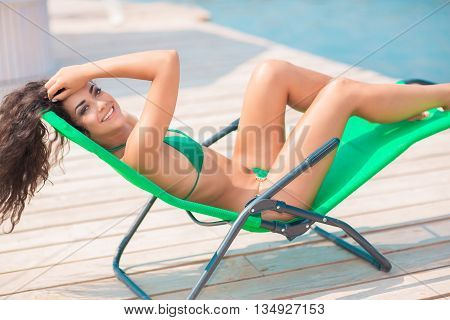 Young attractive woman in swimwear posing in caise-lounge on the beach.