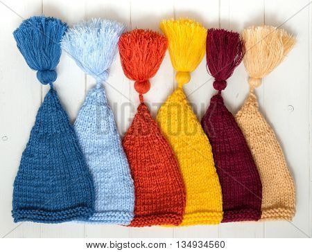 colorful baby knitted hats folded in row on white painted table, top view