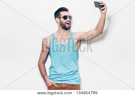 Capturing fun. Happy young handsome man making selfie while standing against white background