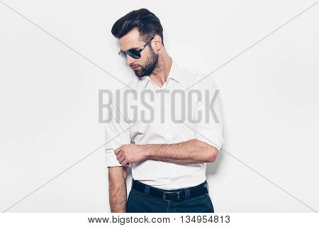 Used to look perfect. Handsome young man in white shirt adjusting his sleeve while standing against white background