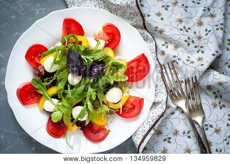 Fresh summer salad. Salad from tomatoes agaricus lettuce pepper and mozzarella. Grey beton background.