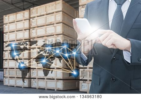 Double exposure of businessman using smart phone network connection world map , transportation port and blurred cargo warehouse background international transportation trading business concept