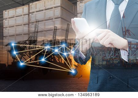 Double exposure of businessman using smart phone network connection world map , transportation port and blurred cargo warehouse background international transportation trading business concept