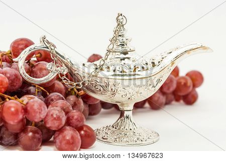 Silver Aladdin's magic lamp and red grapes. Ramadan Eid concept background