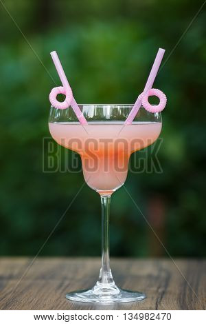 Glass of cold pink cocktail with straw on green background bokeh