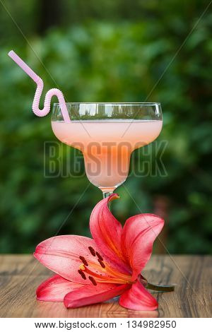 Glass of cold pink cocktail with straw on green background bokeh
