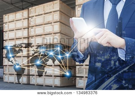Double exposure of businessman using smart phone network connection world map by NASA city of business center and blurred cargo warehouse background international transportation trading business concept