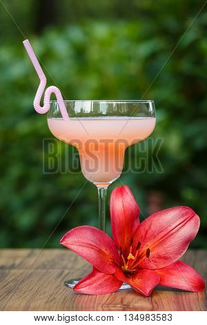 Glass of cold pink cocktail with straw on green background bokeh