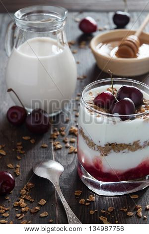 A glass of cherry yoghurt with muesli honey and a jar of milk